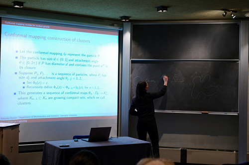 Colour photograph of Prof. Turner giving her talk, with display screen and blackboard