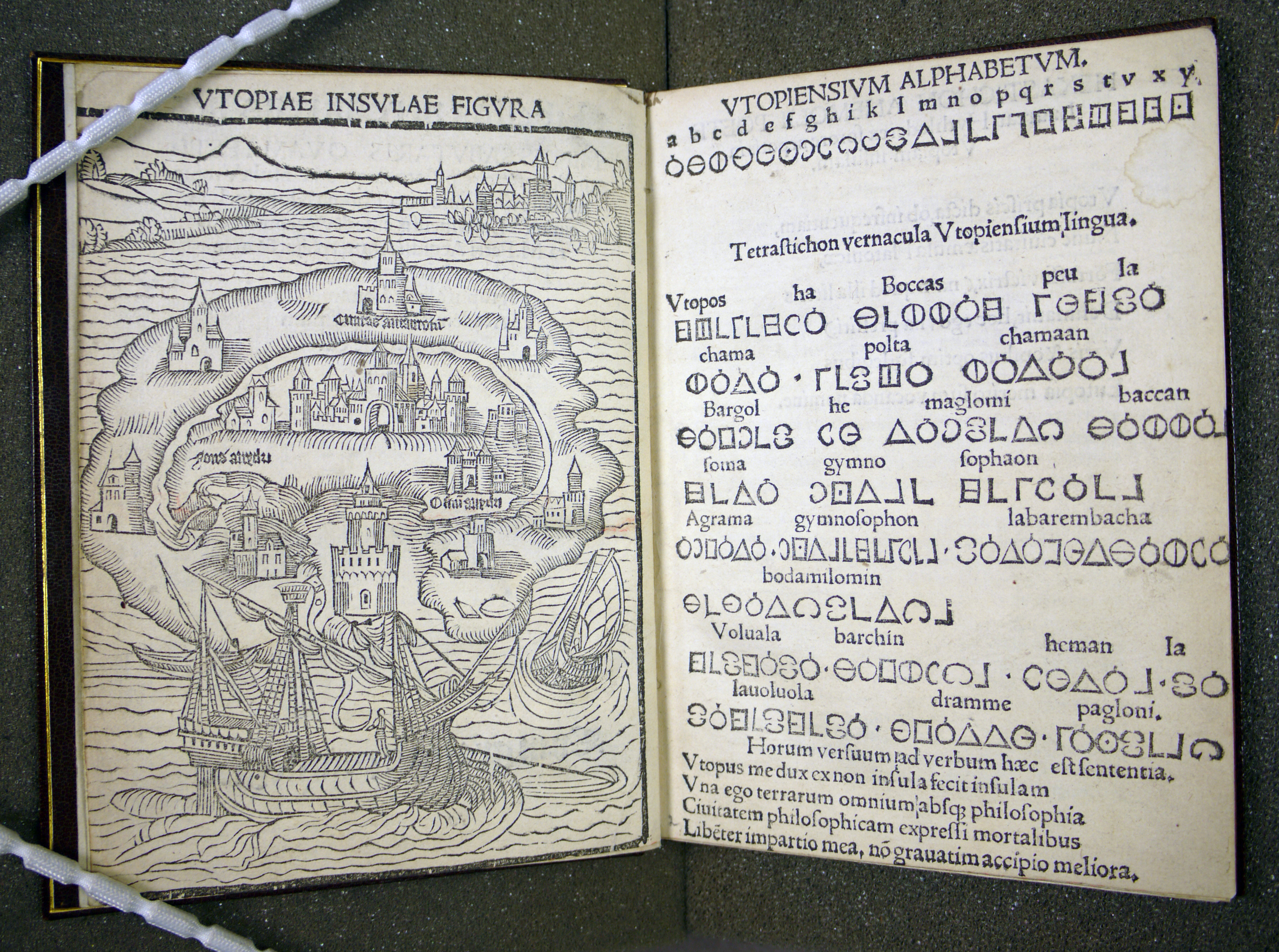 The frontispiece of Thomas More's Utopia. The book is open to a double-page spread featuring, on the left, a drawing representing an overview of the island of Utopia and, on the right, a key to the Utopian alphabet, accompanied by text in Latin. 