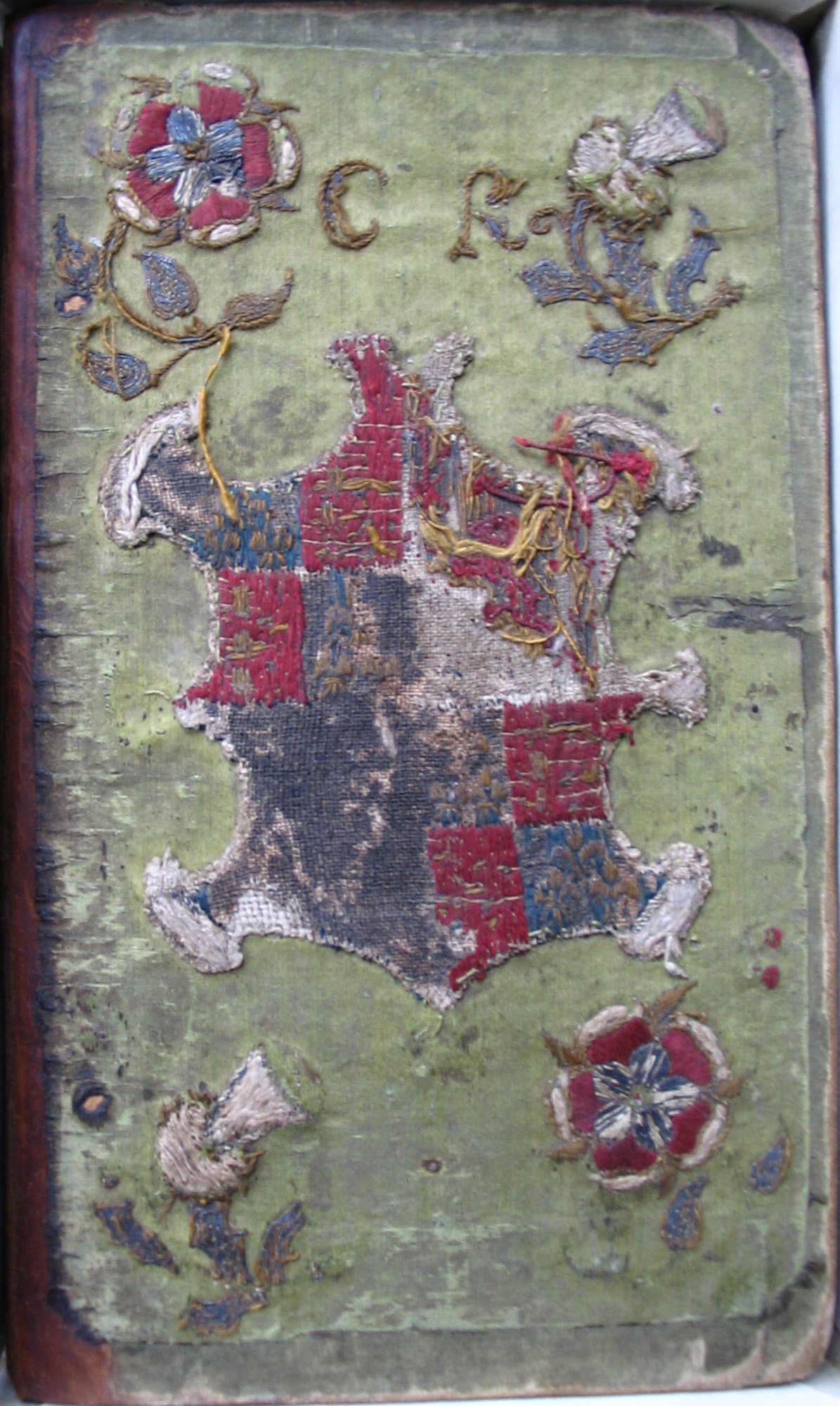 A book bound in green fabric embroidered with flowers, a coat of arms, and the initials C R.