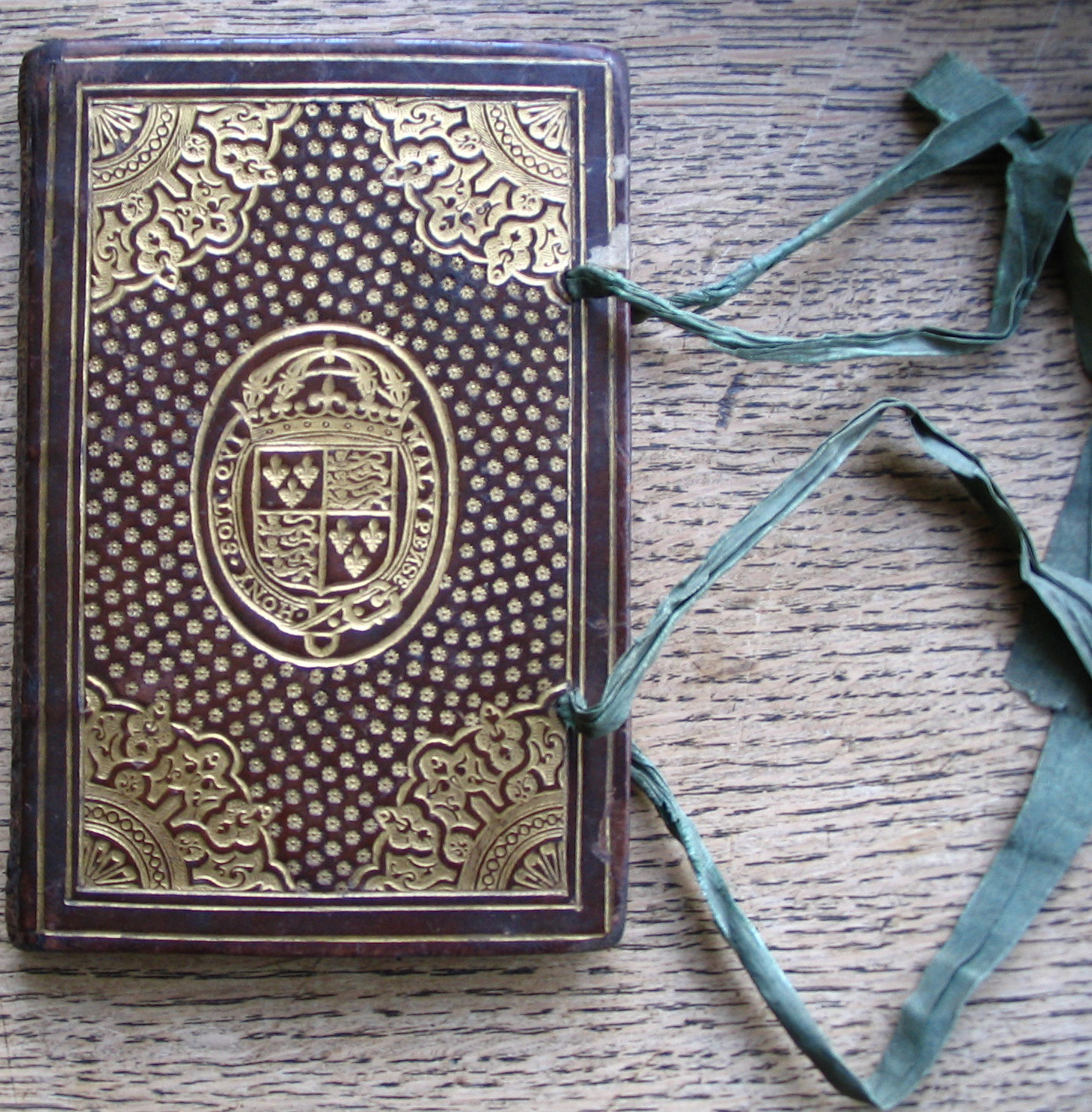 A small book, in an ornate red and gold binding, with turquoise ribbons.