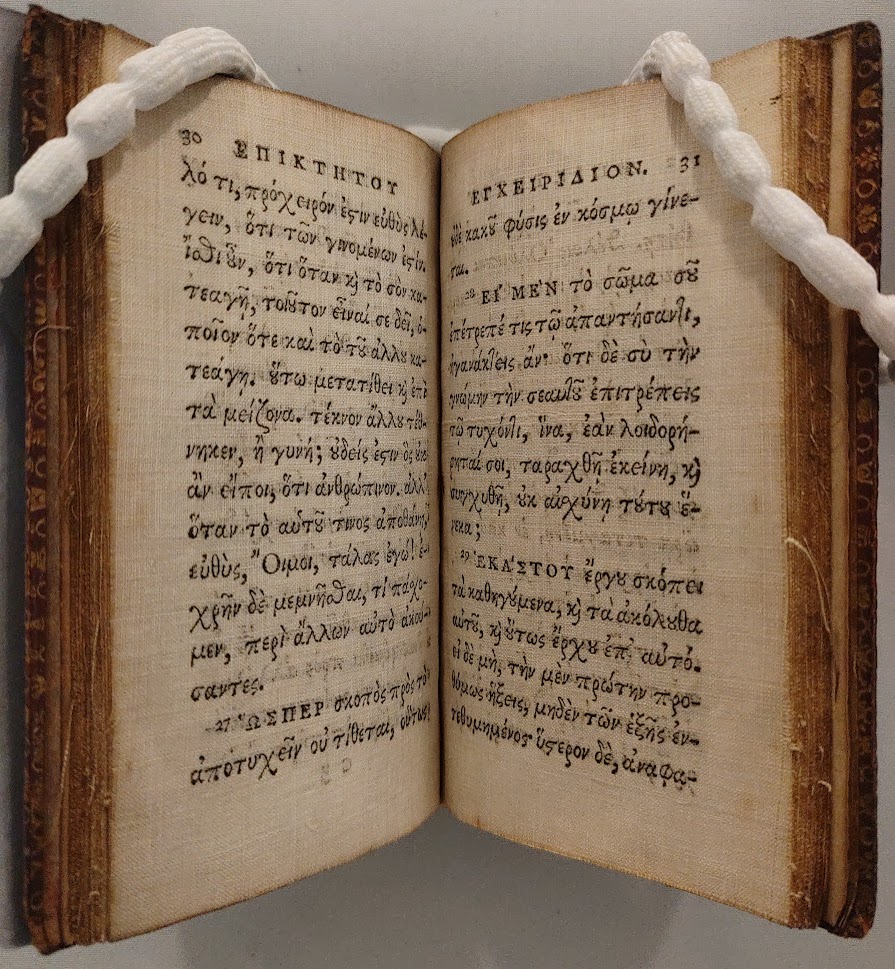 A book printed in Classical Greek, with the pages held open by weights.