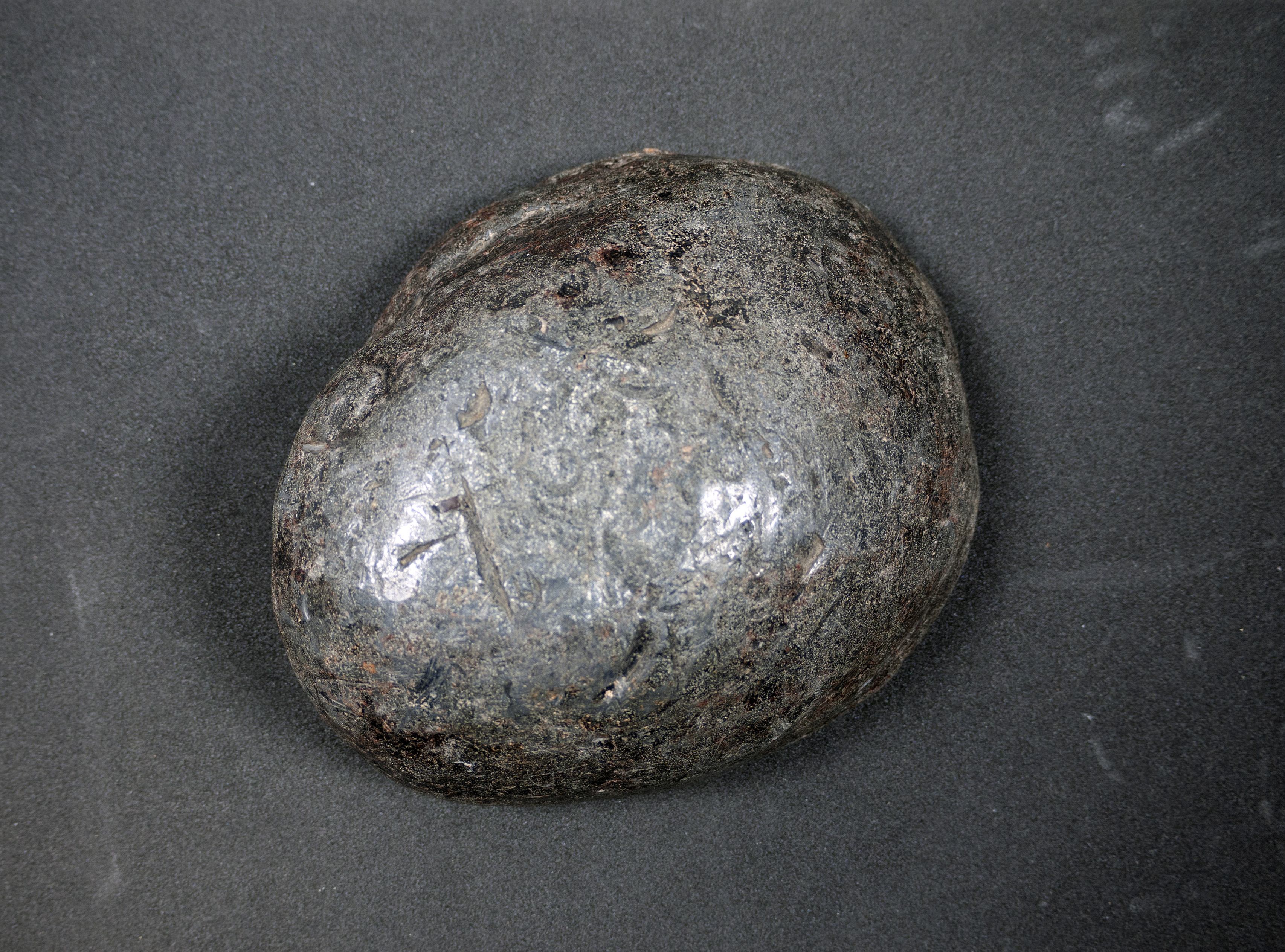 An irregular dome-shaped lump of lead on a cushion, viewed from above.