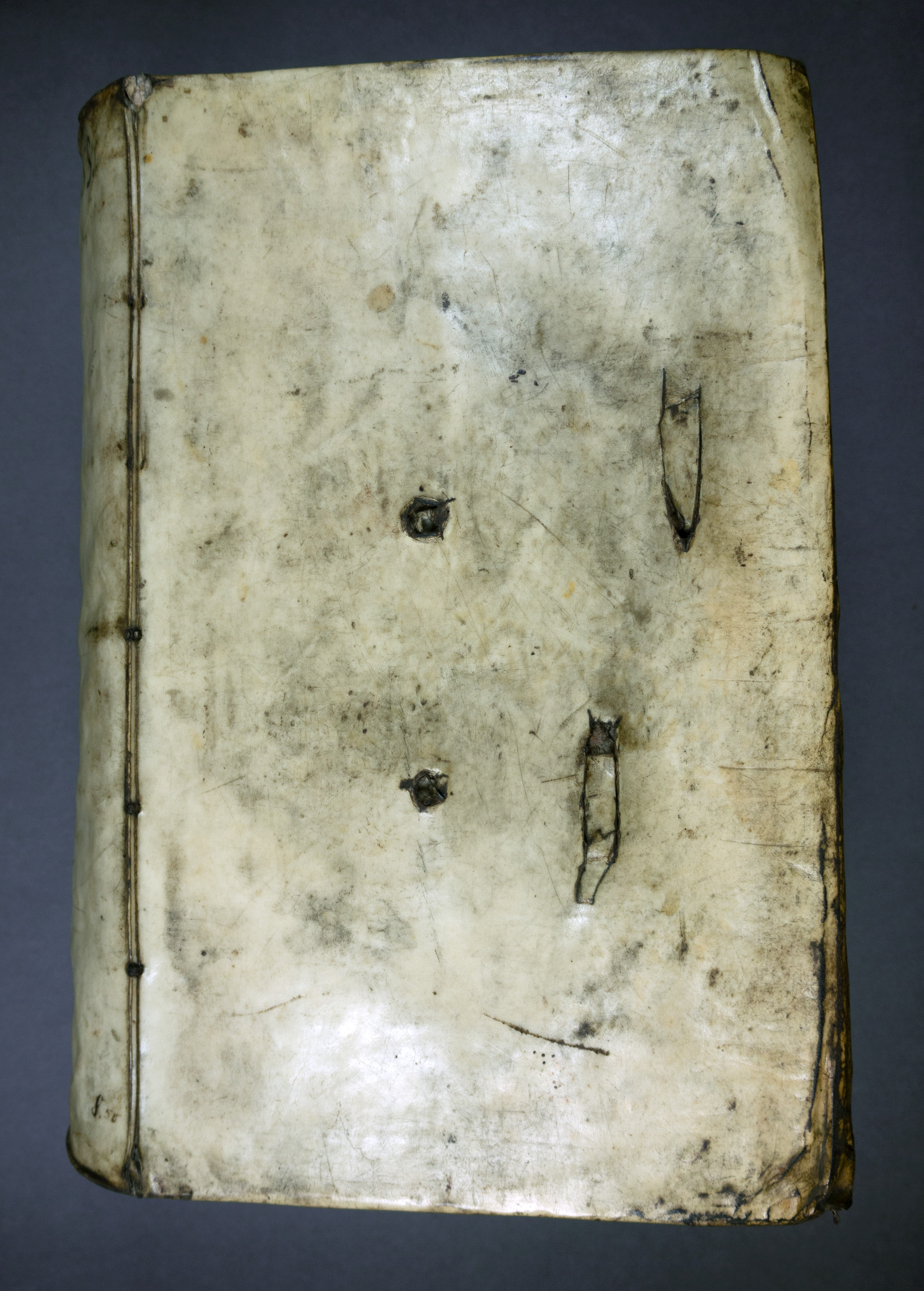The front board of a large book with a pale leather binding. The binding bears four rough holes which, although this is not quite visible in the picture, run all the way through the volume.