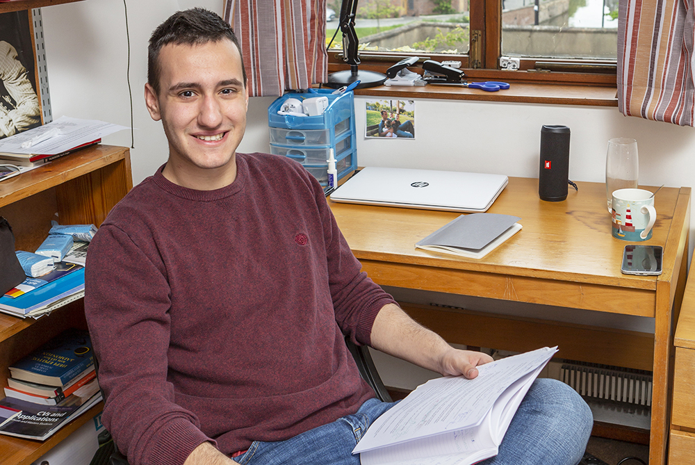 A student sits at his desk in his room