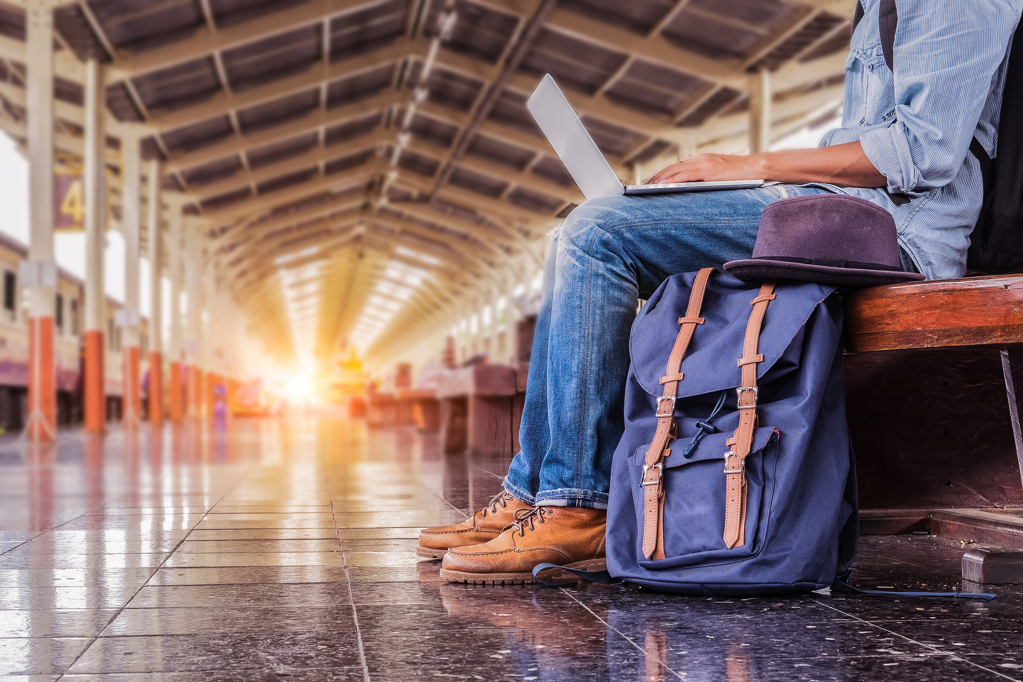 A person sits at a train station working on their laptop