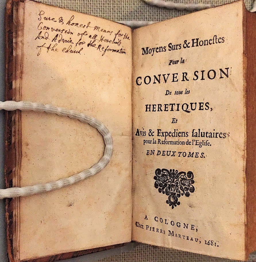 A book held open with weights, showing a title page in French, with a handwritten note translating it into English.
