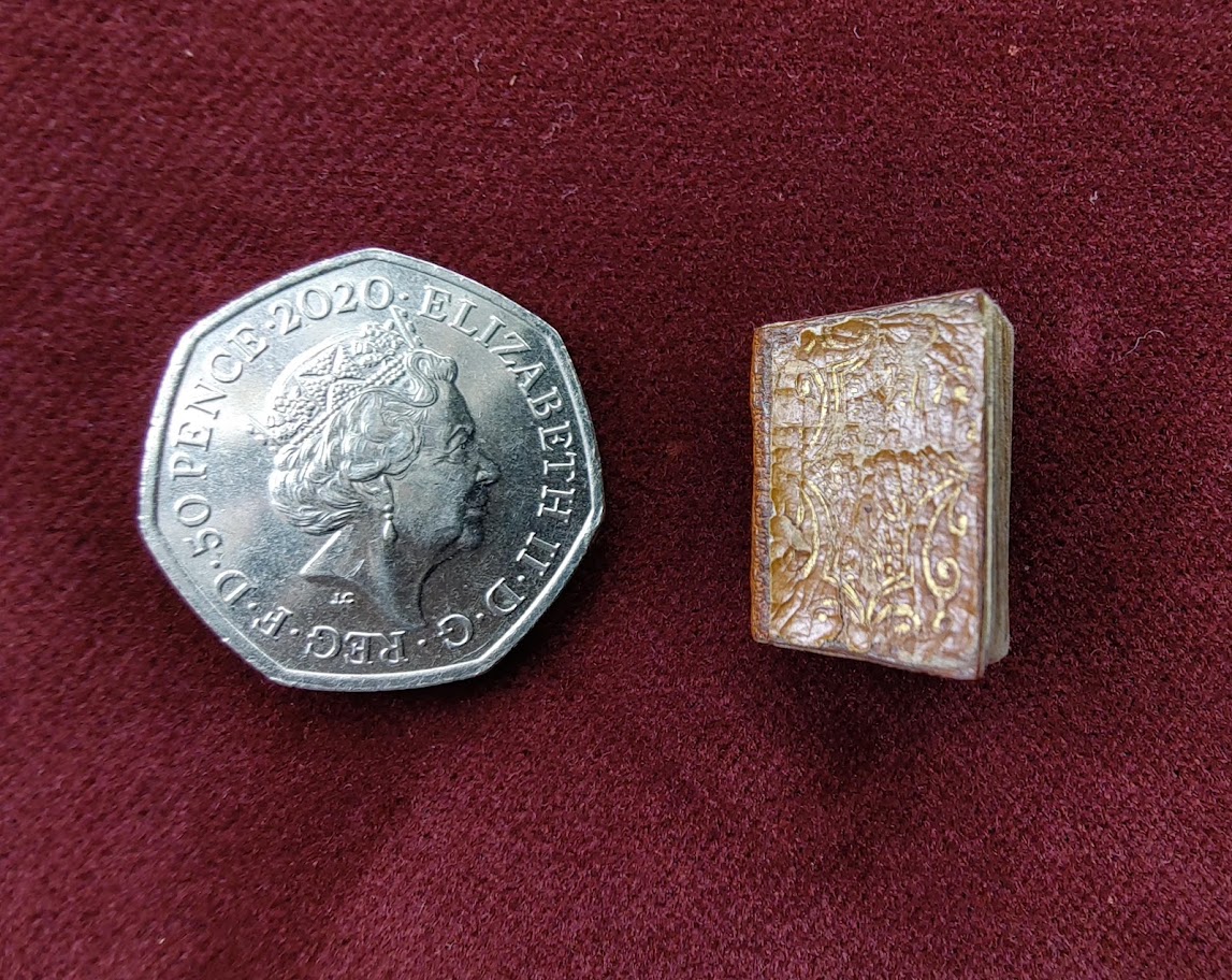A very tiny book next to a fifty pence piece for scale.